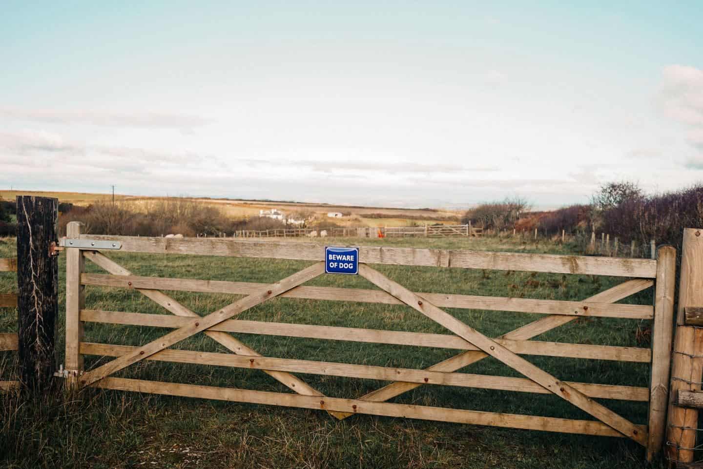 A gate in a field with a beware the dog enamel sign on it