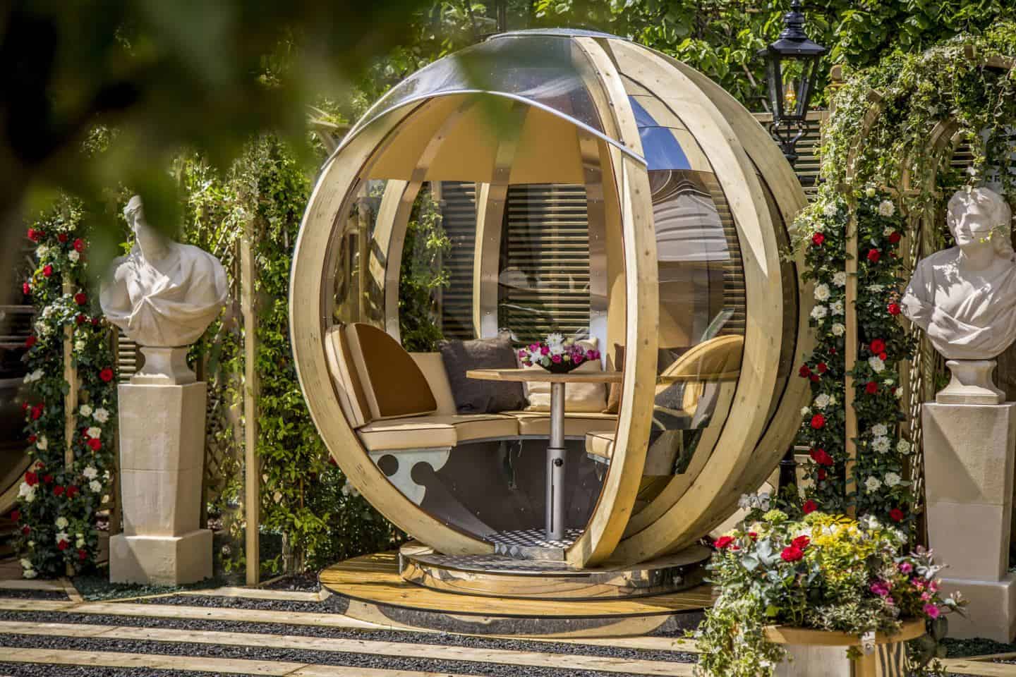 A rotating lounger garden pod flanked by two marble busks on plinths.