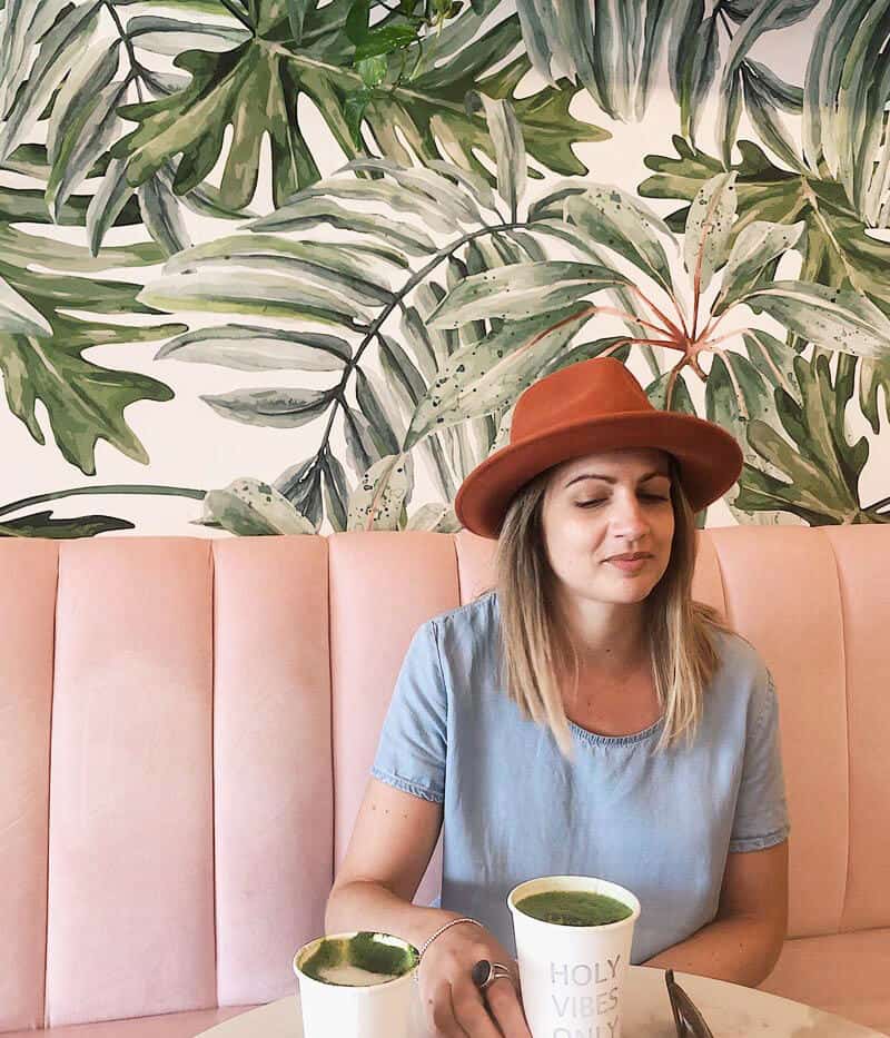 Michelle founder of Greenlili, sat in an upholstered pink bench seat with botanical wallpaper behind