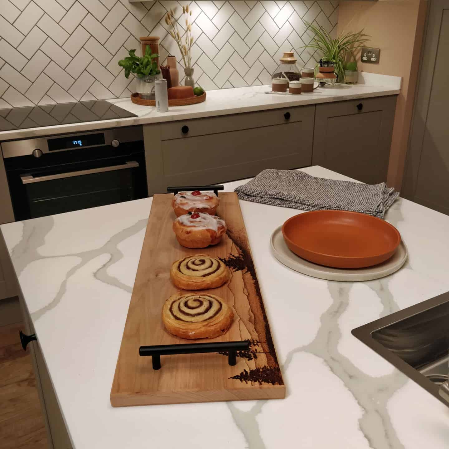 Biophilic kitchen designs provide a multi-sensory experience through natural materials and textures. Here kitchen accessories are displayed on a marble effect worktop.