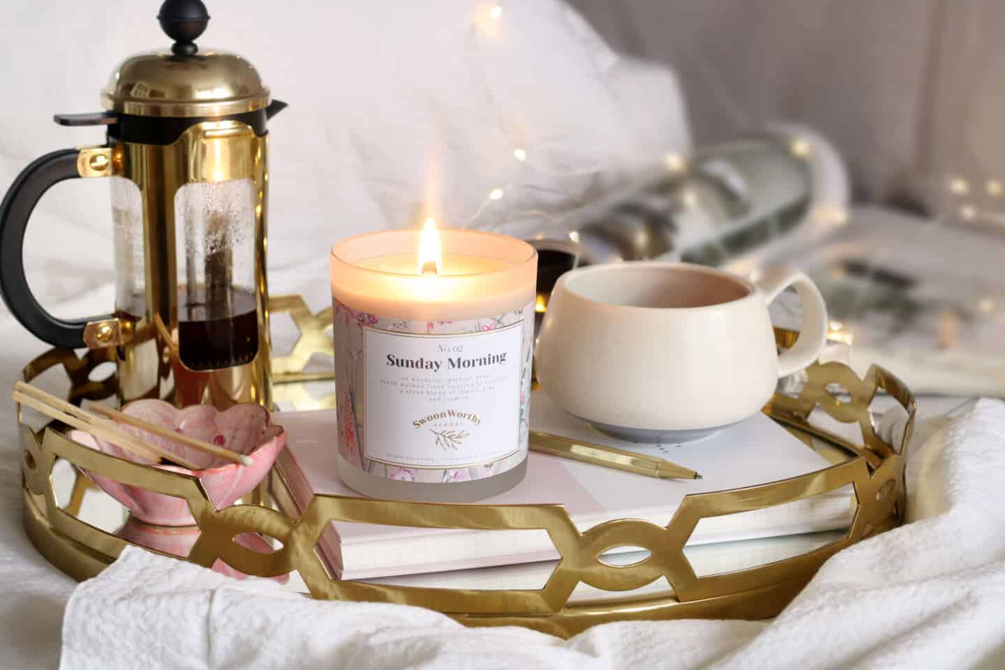 A tray on a bed featuring a cafietiere, a coffe cup and a luxurious scented candle