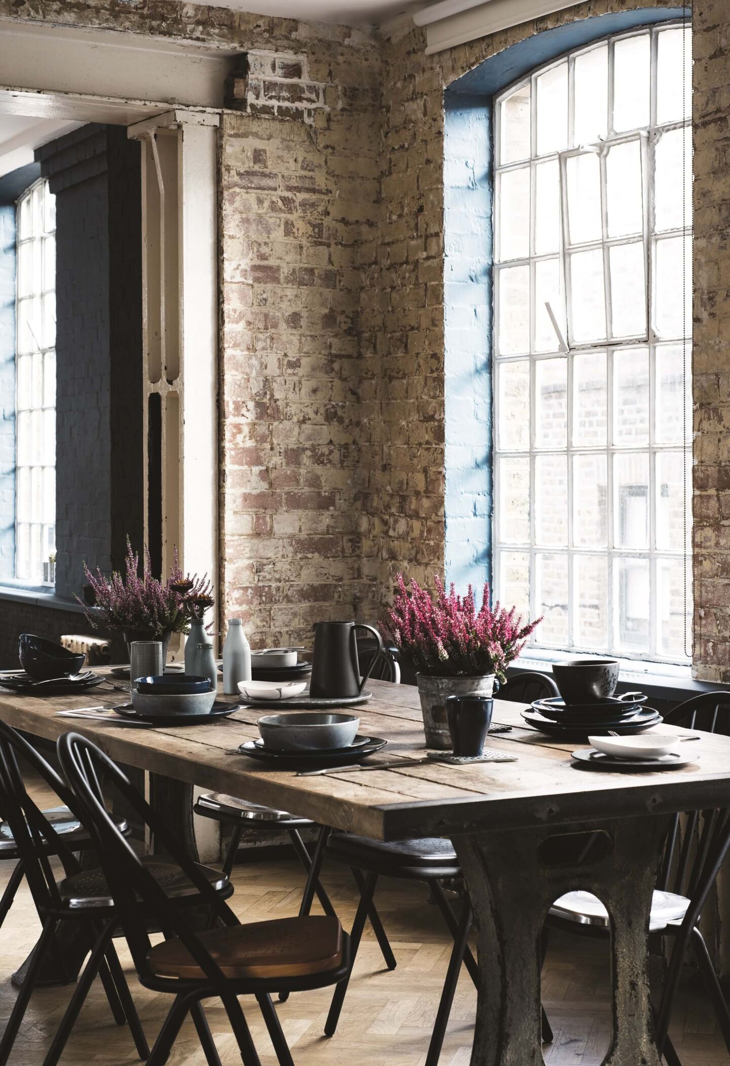 Industrial loft-style dining room. A large rectangular dining table with 6 chairs around situated in front of industrial windows