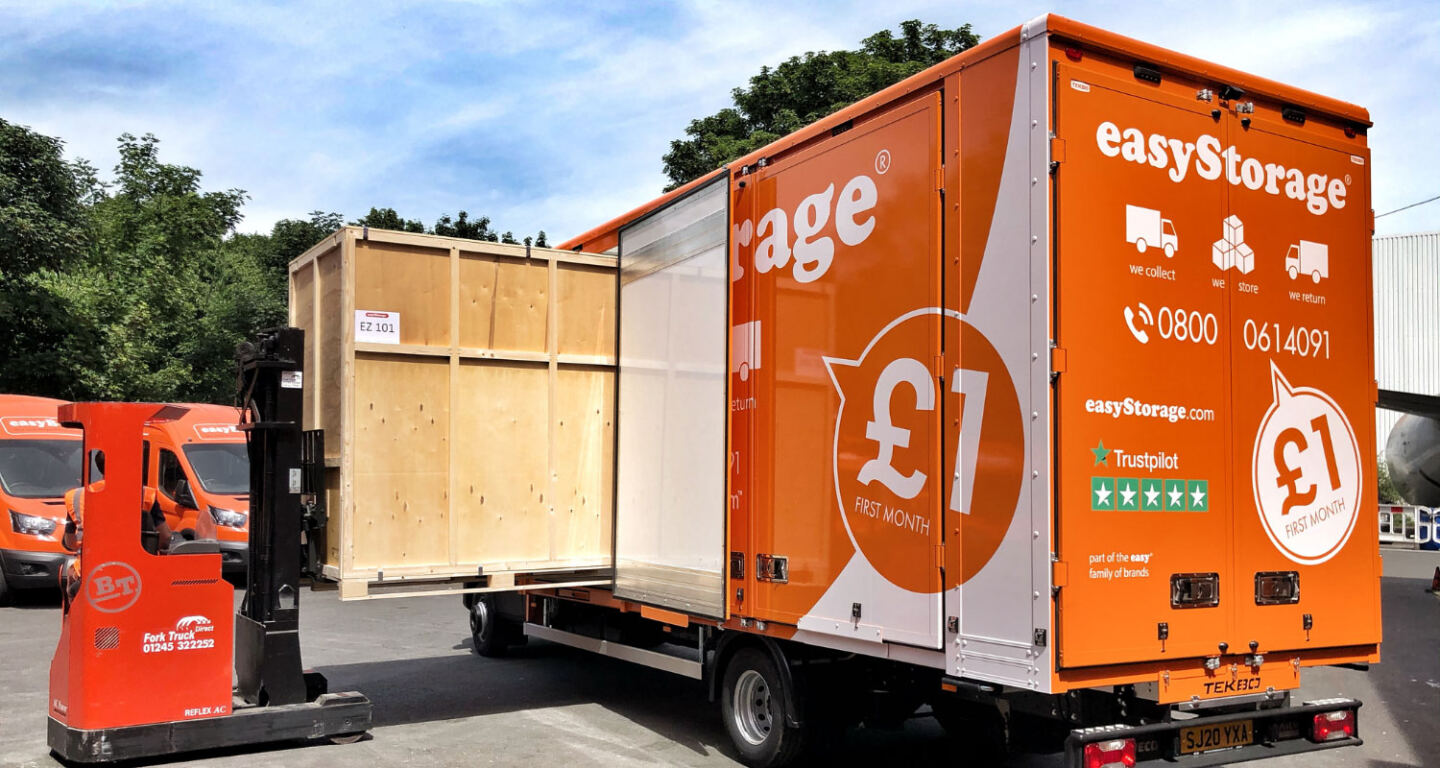 A wooden crate is being unloaded from an big orange easyStorage van ready for self-storage