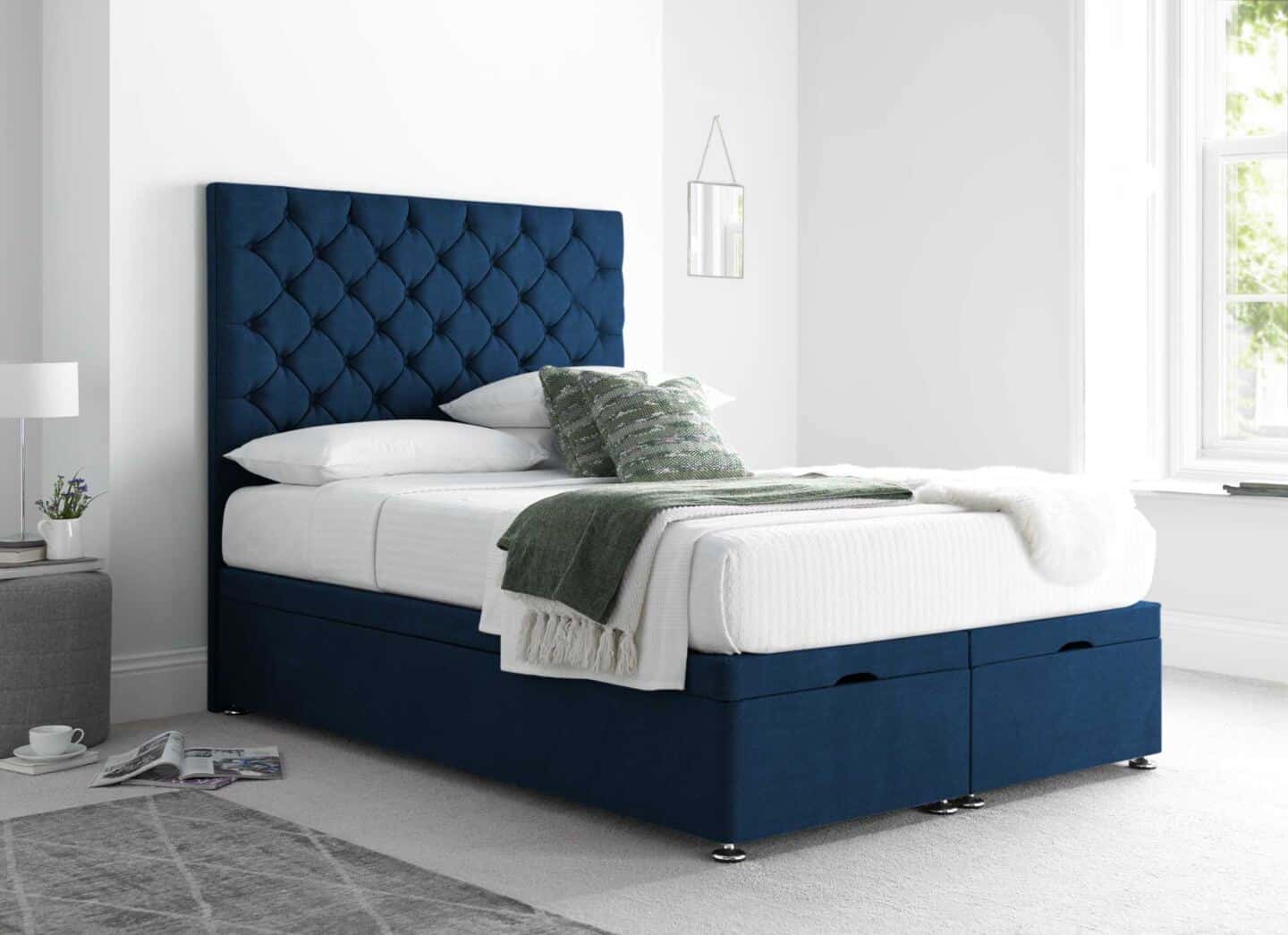 A blue ottoman bed with white bedding    and a tall tufted headboard in a large white airy bedroom