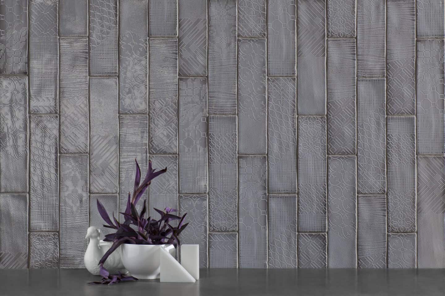 Grey textured tiles with a bowl of purple flowers in front