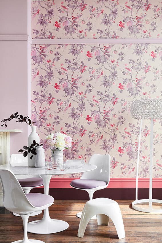 A dining room with pink floral wallpaper. The skirting board is half pink and half purple. Image c/o Little Greene