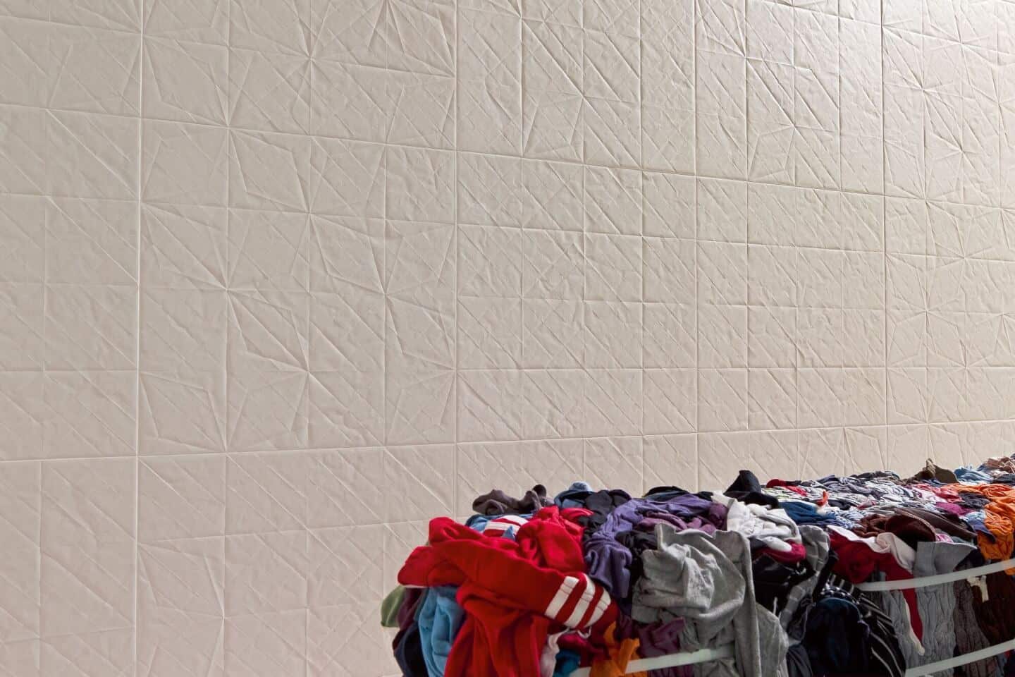 White textured wall tiles. A pile of laundry is in the foreground