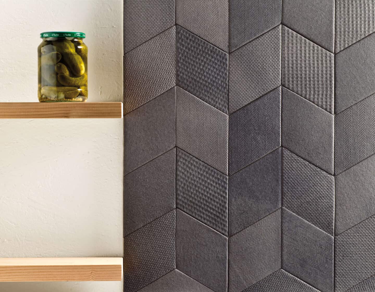 Black textured wall tiles next to two shelves. A jar of pickles is on one of the shelves.