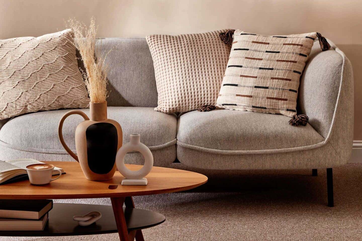 A coffee table in front of a grey sofa. Cushions from the Primark Homeware range for SS22 are on the sofa and a selection of decorative accessories are on the table 