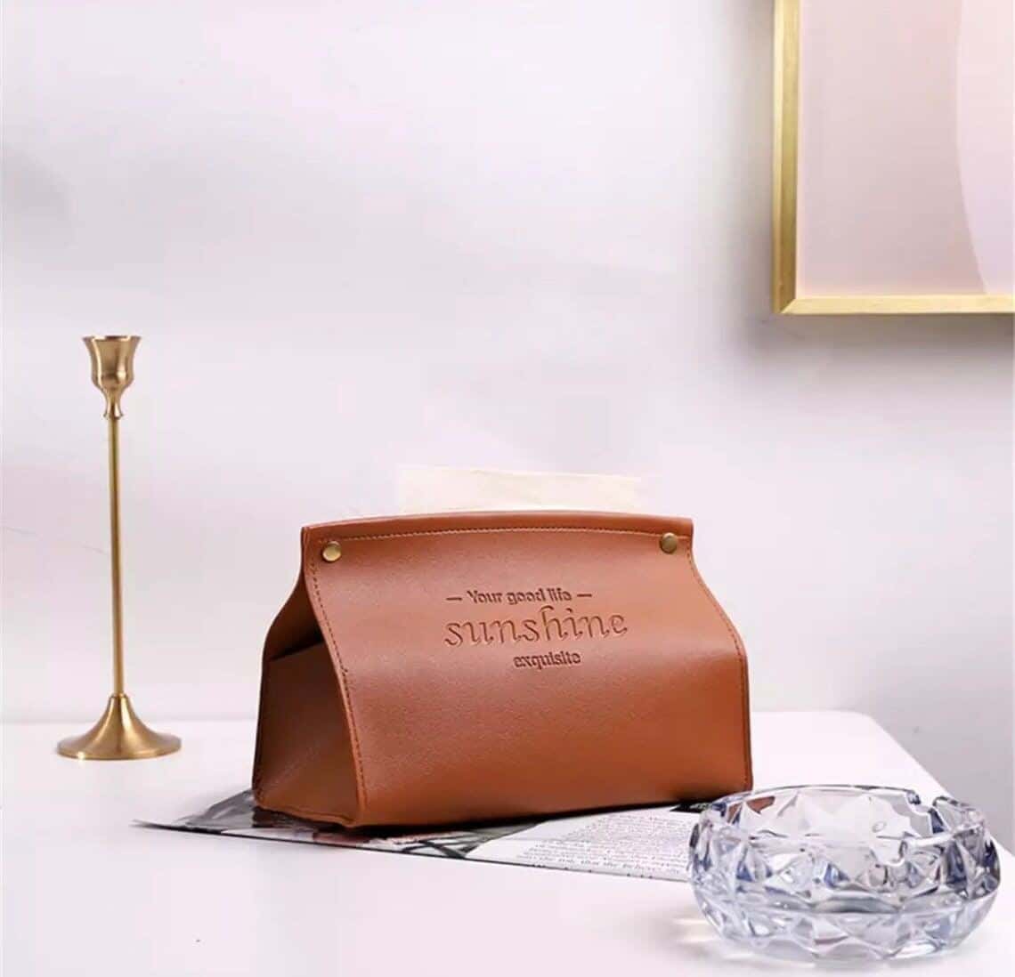 A brown leather pu tissue box on a grey surface with a candle stick nearby
