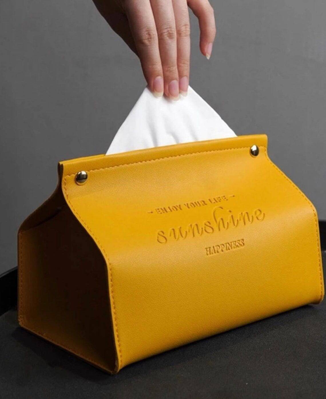 A hand pulls a tissue from a yellow pu leather tissue box