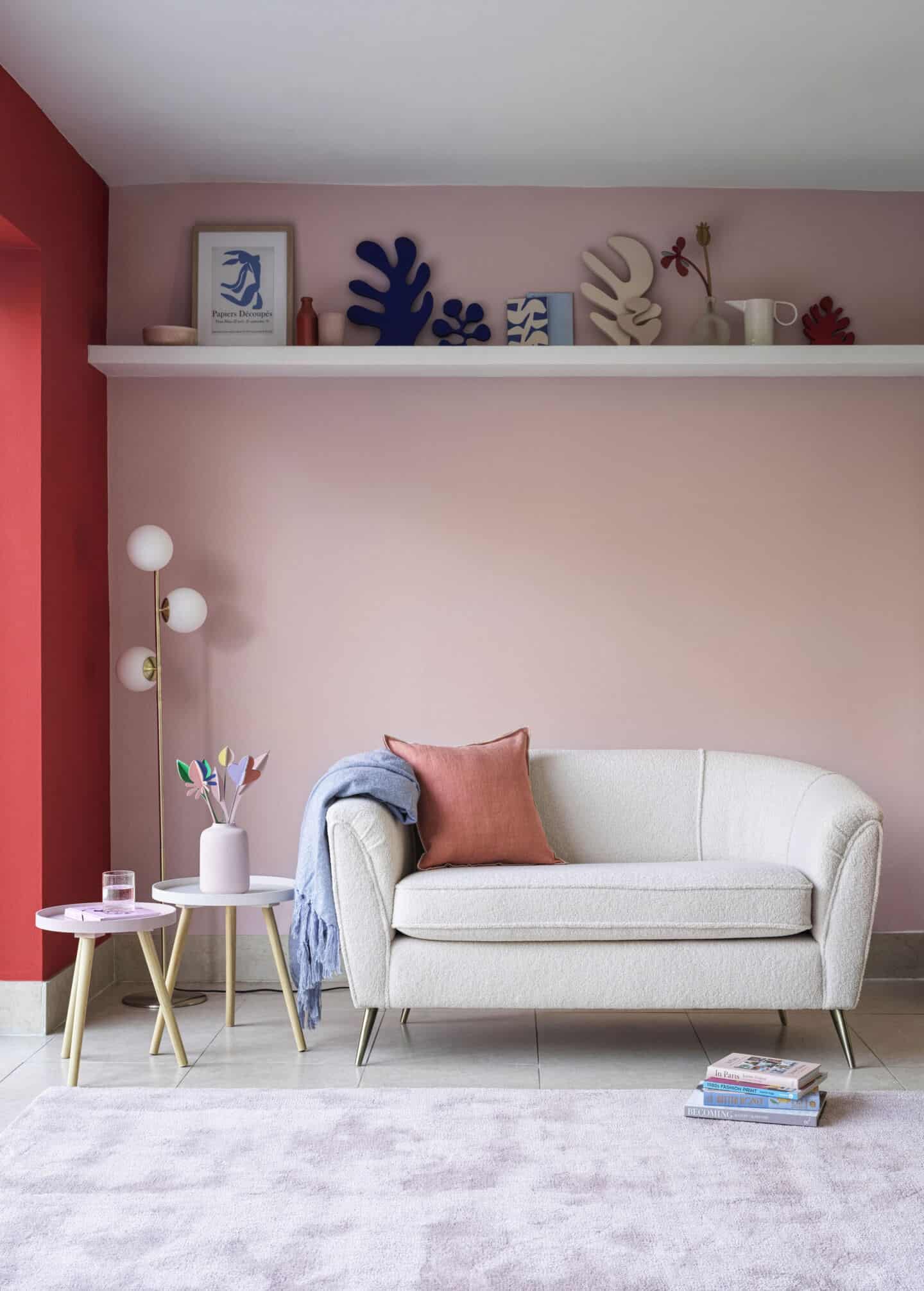 A small white curved boucle sofa in front of a pink wall 