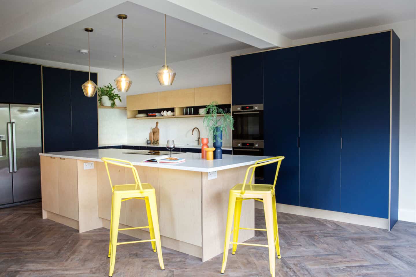 A navy blue kitchen with a plywood kitchen island and yellow bar stools