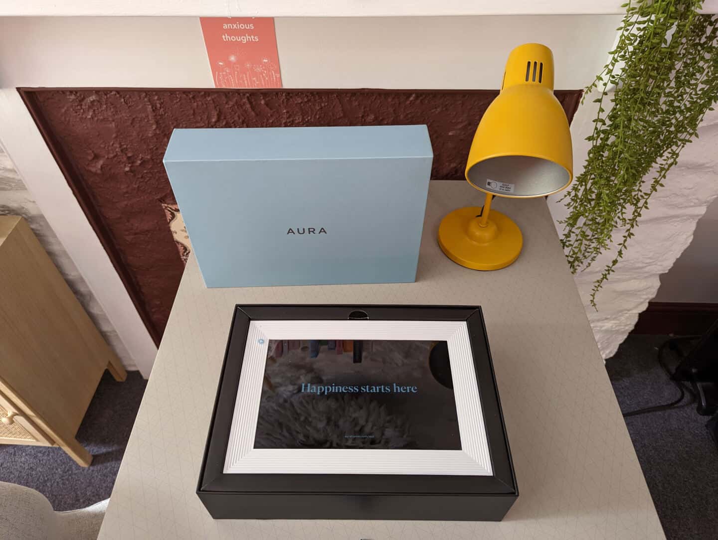 An open blue box on a desk next to a yellow lamp. The box contains a digital photo frame