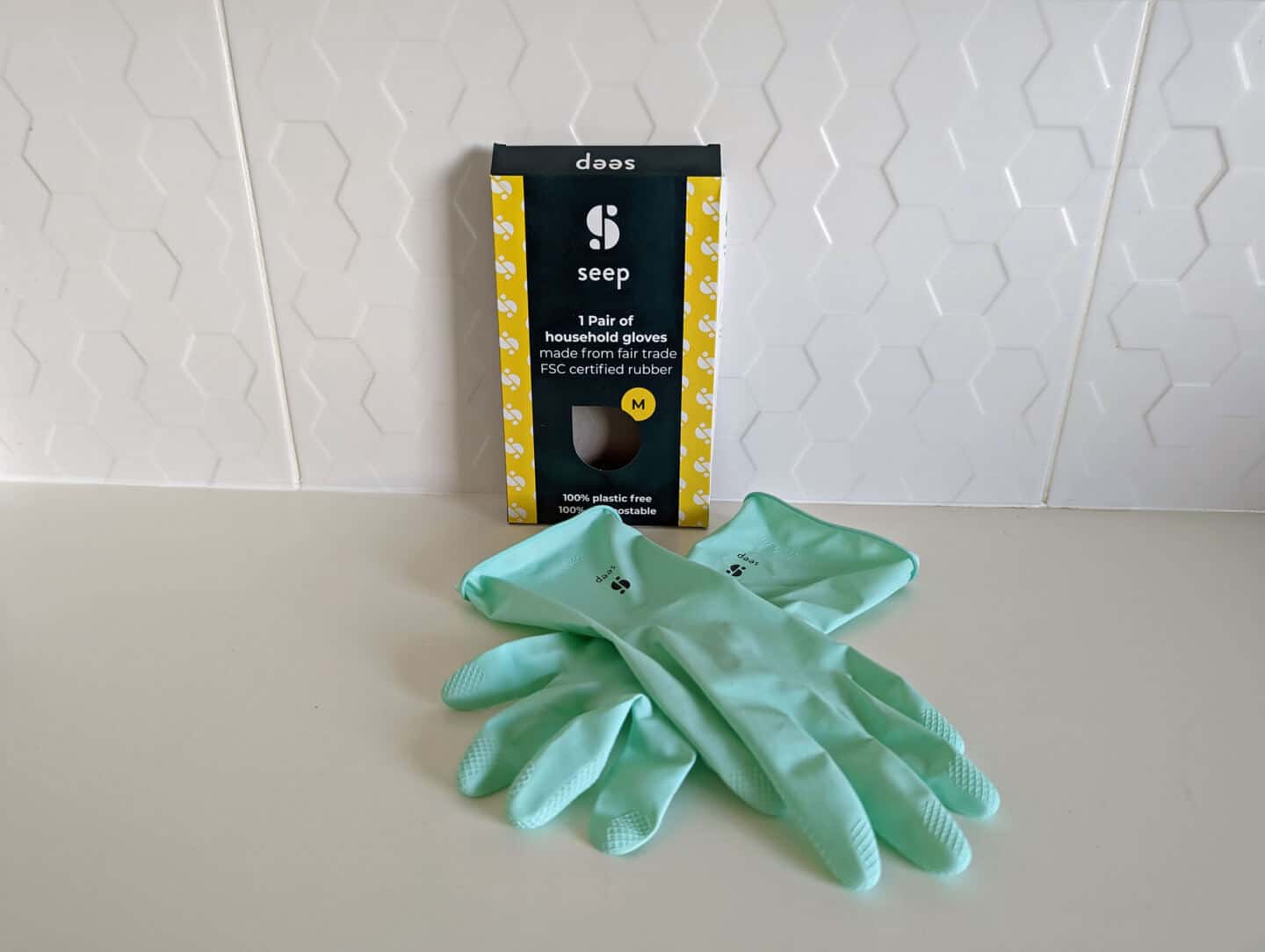 A pair of natural rubber gloves from Seep on a white worktop with white tiles behind 