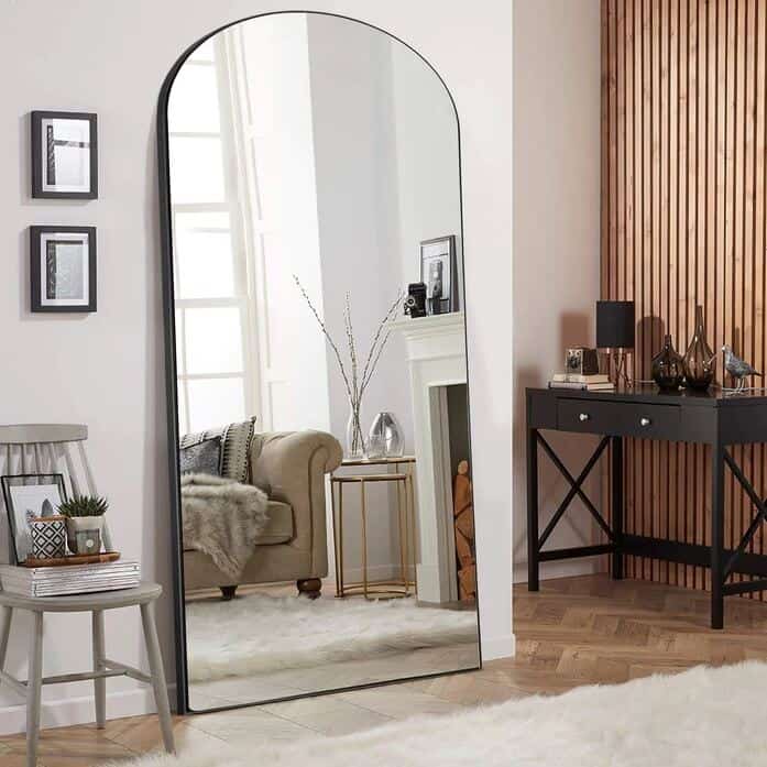 Large floor standing arched mirror in a living room reflects natural light at home 