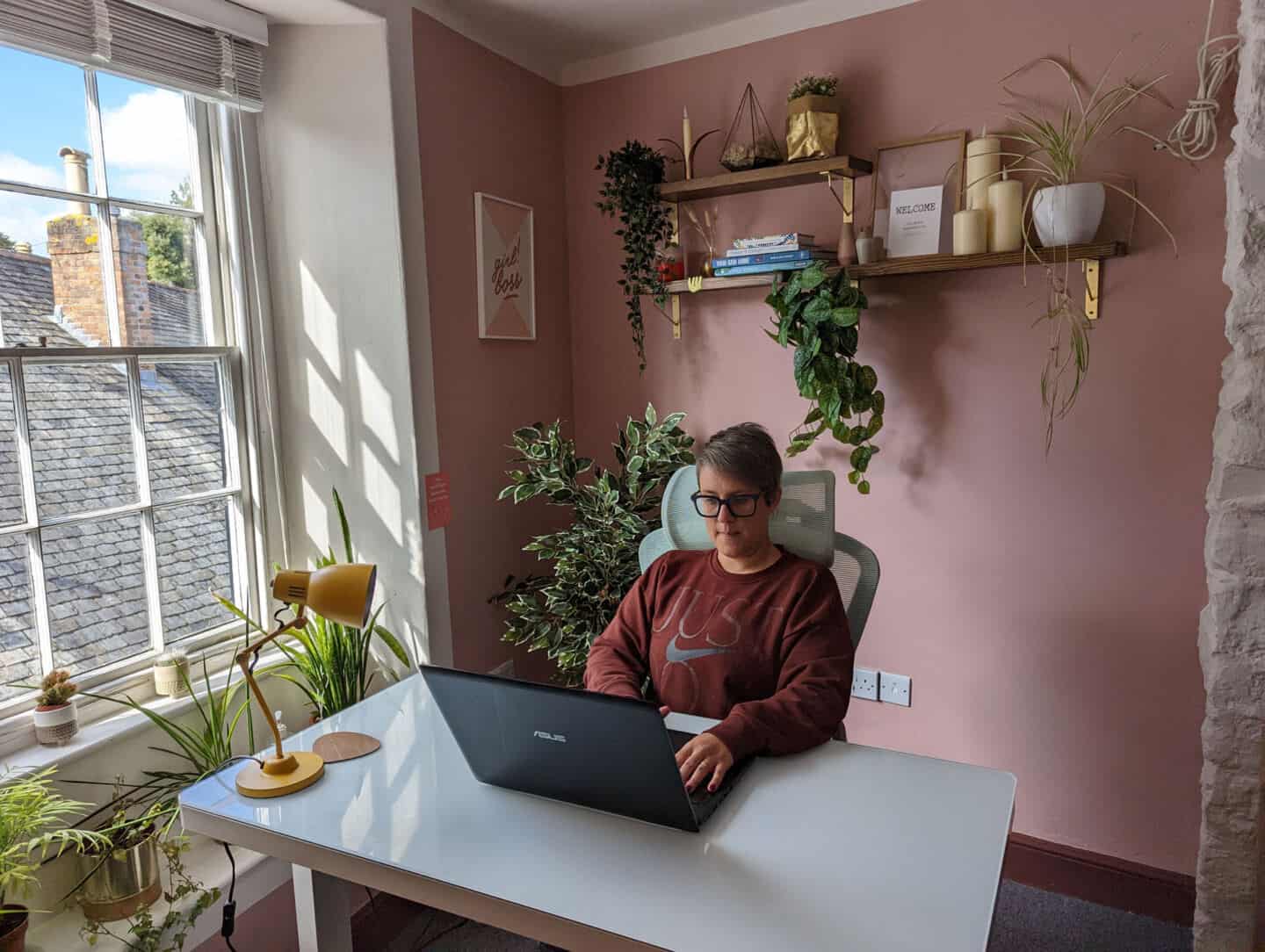 A woman sat at a desk working on a laptop in a pink office.