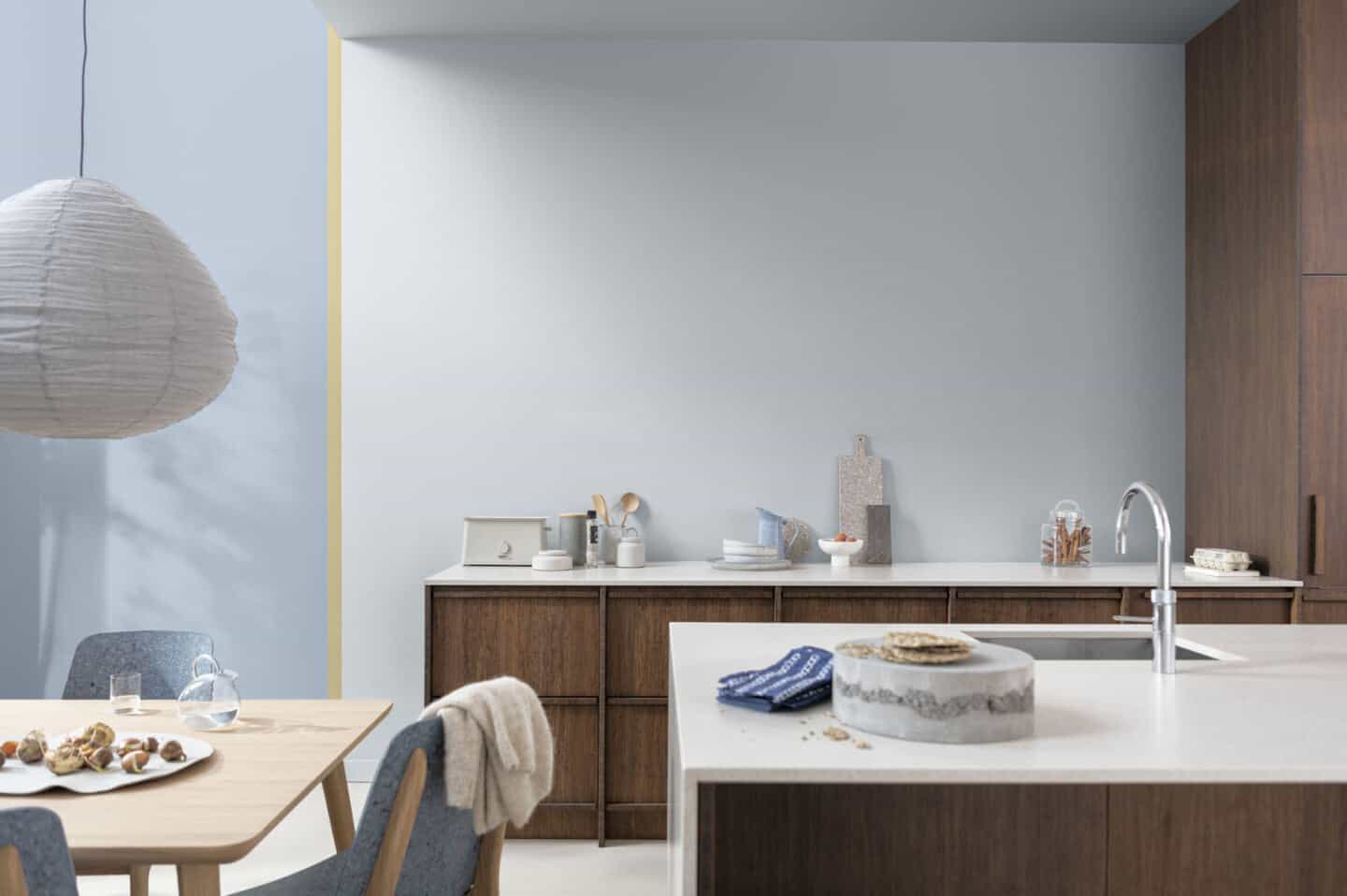 A kitchen in dark wood with white waterfall worktops and blue walls
