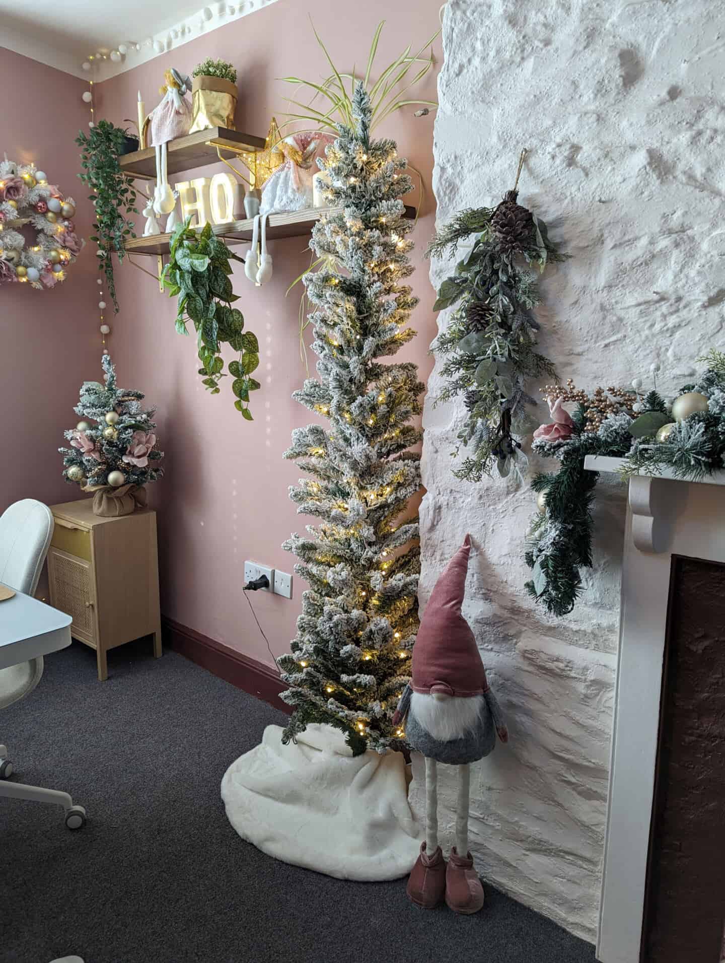 Ein Gonk steht neben einem beflockten Weihnachtsbaum in einem rosa Home Office