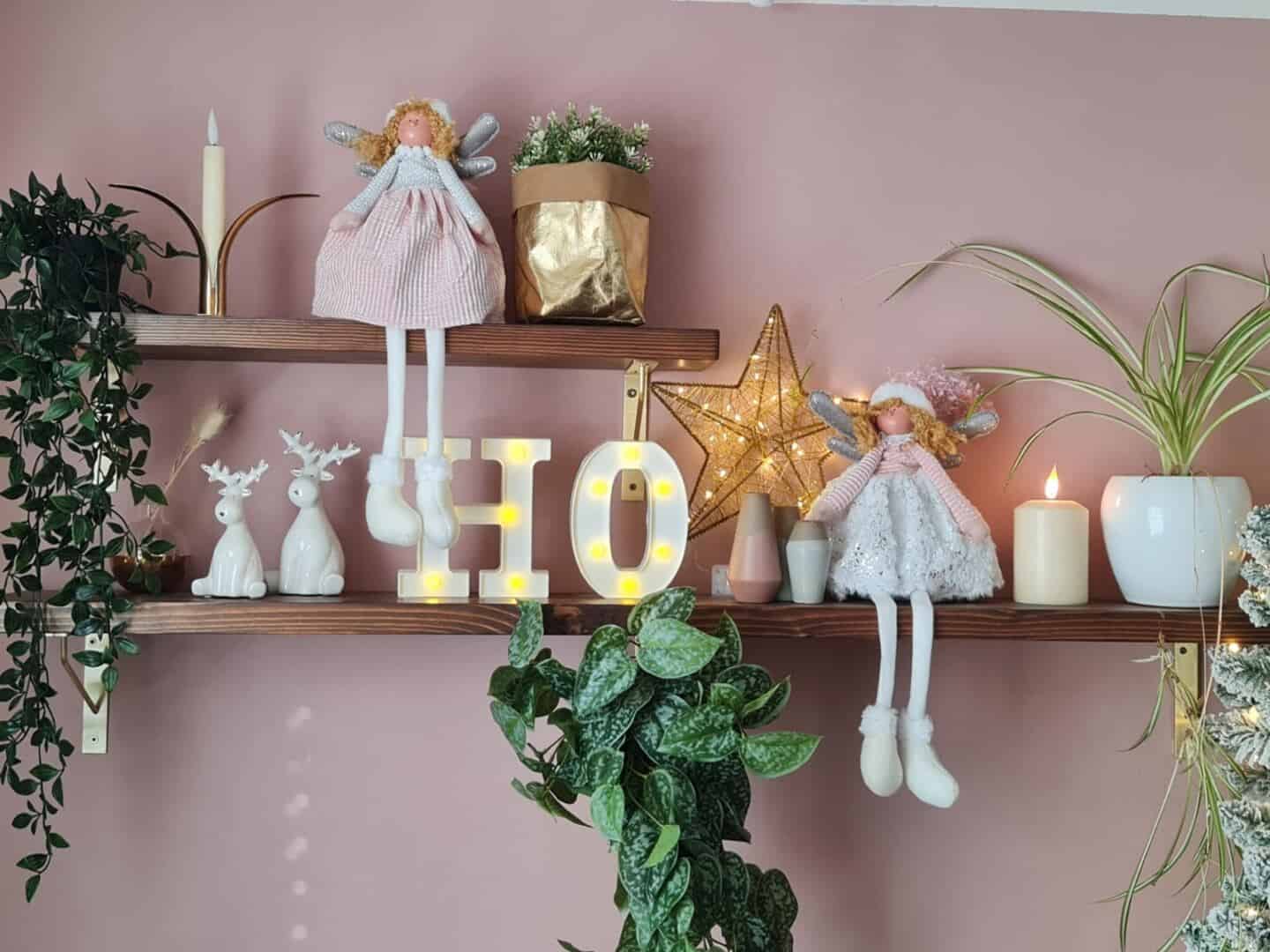 Dark wood shelves in a pink home office adored with Christmas ornaments and candles