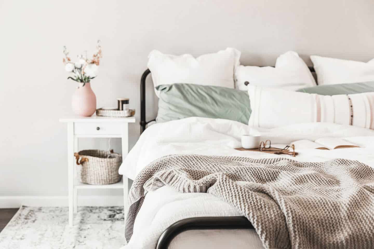 a metal frame bed piled high with pillows and a woollen blanket draped over the end.
