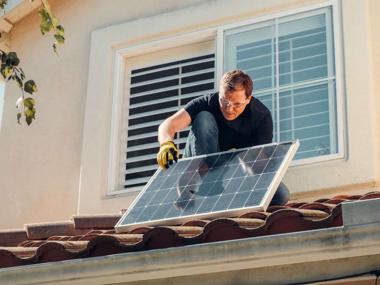 Ein Mann installiert Sonnenkollektoren auf einem Dach, um die Heizkosten zu senken
