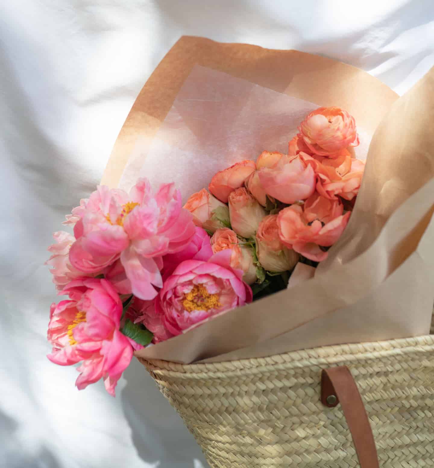Pink Peony flowers wrapped in paper inside a woven palm leaf bag