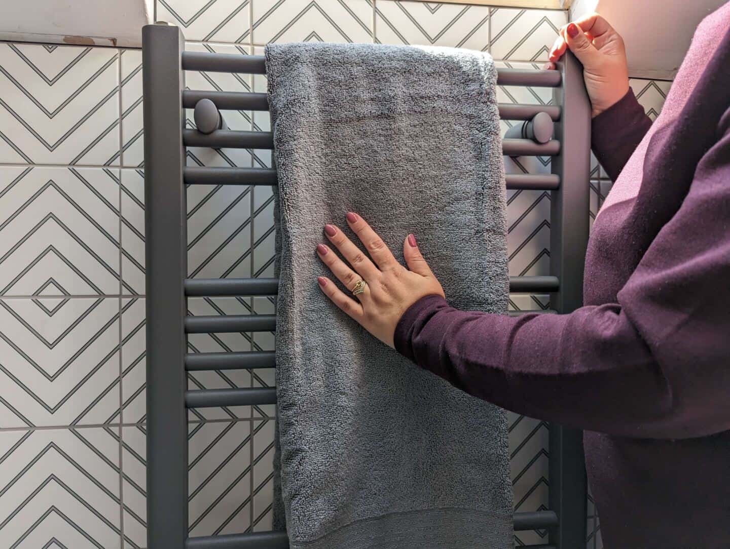 Woman strokes a grey bath towel hanging on a matt grey towel radiator 