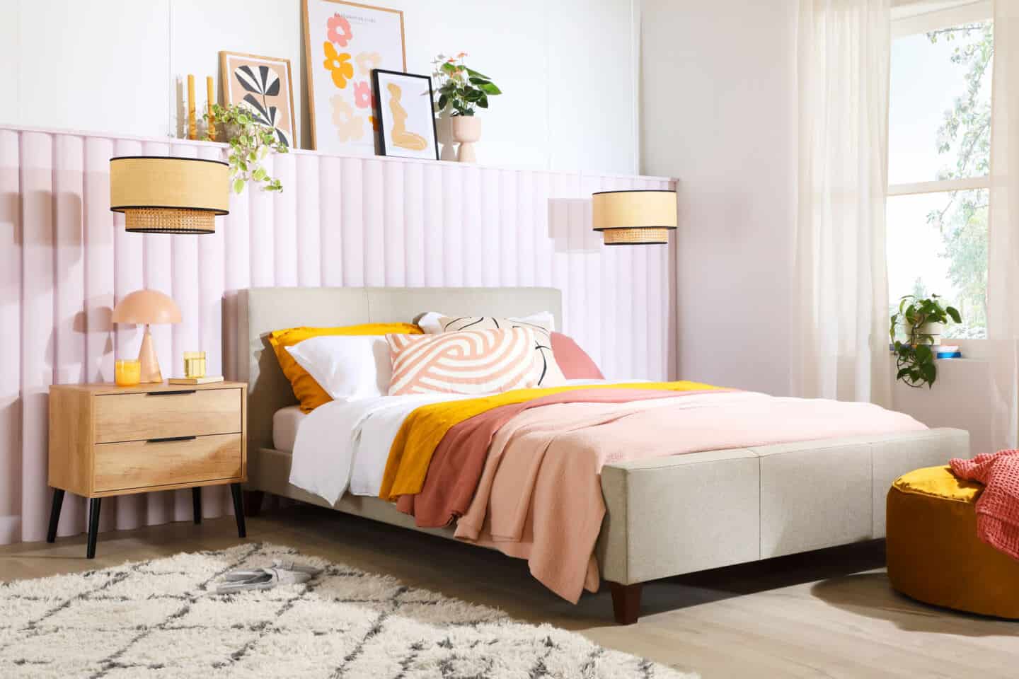 A bedroom in pastel colours with rattan lights hanging down on either side above the bedside tables