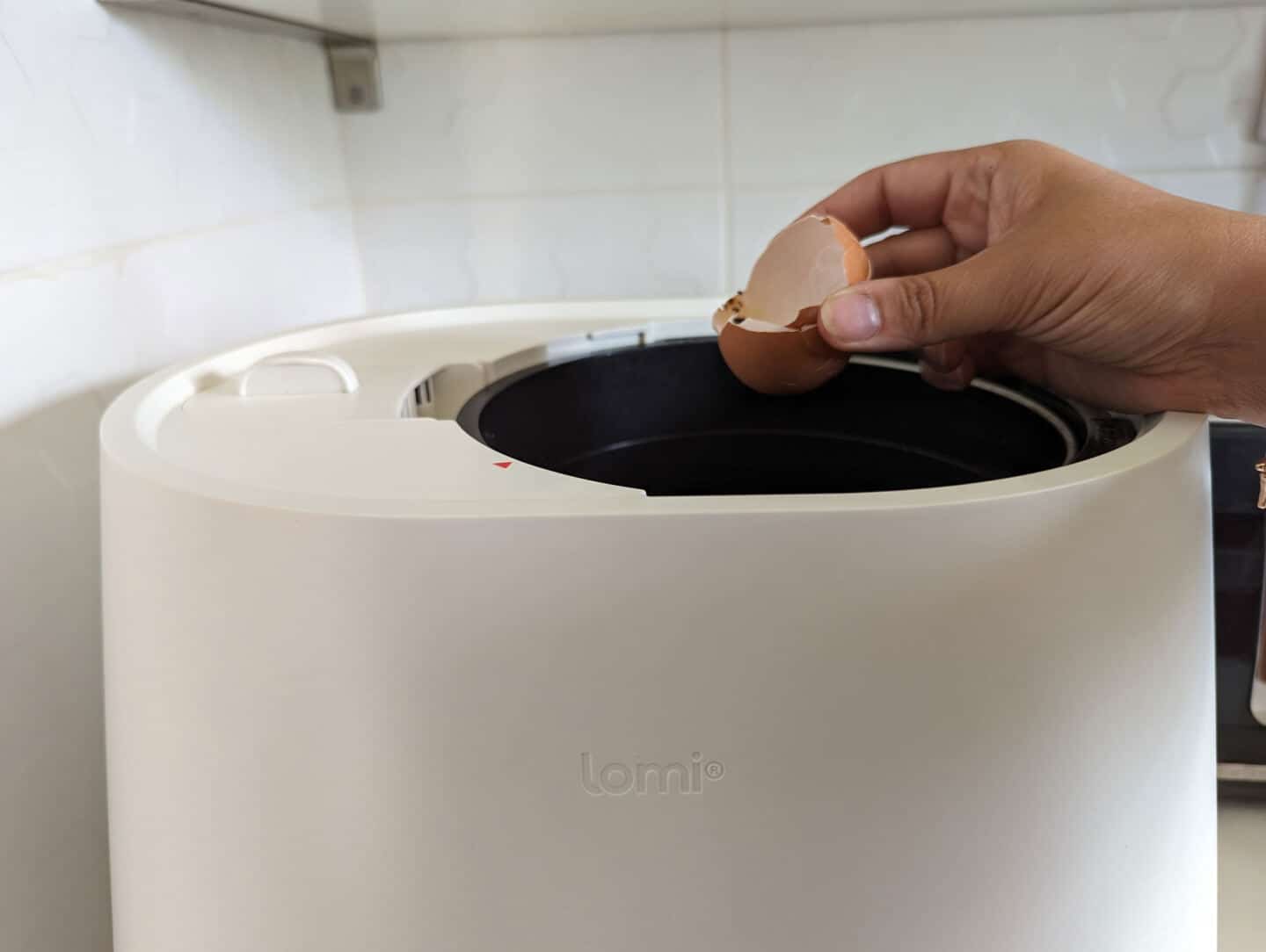 A hand placing an eggshell into the Lomi kitchen composter 