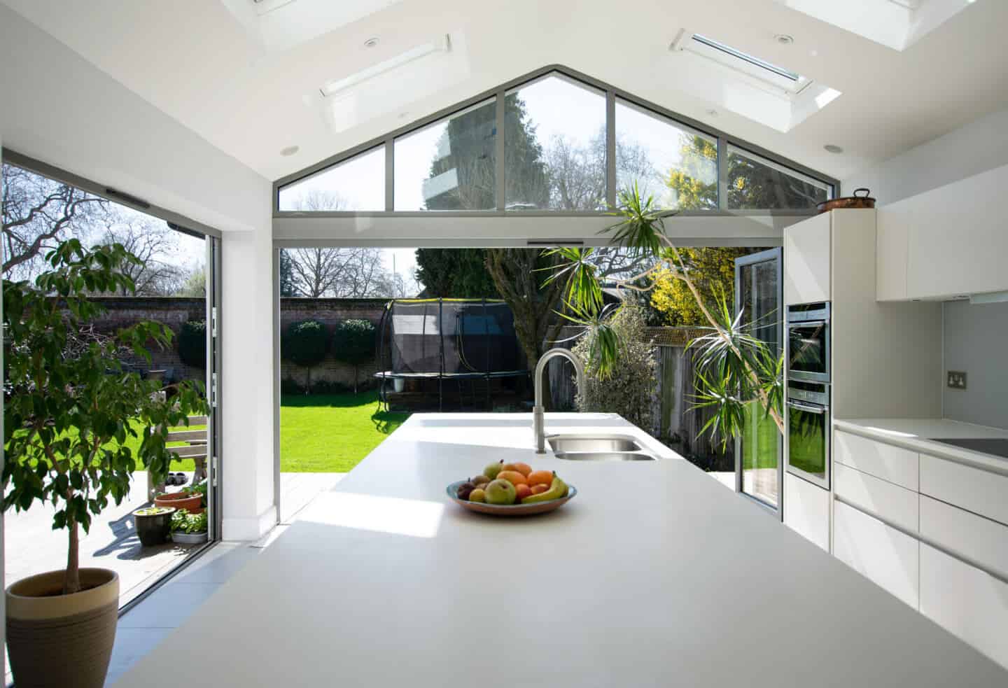 A modern white kitchen with large glass doors leading out to the garden increases natural light at home