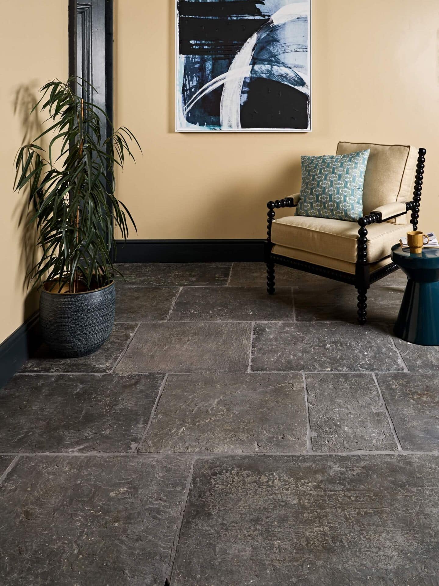 An entryway with dark limestone floor tiles, yellow walls featuring an abstract piece of framed art and a plant