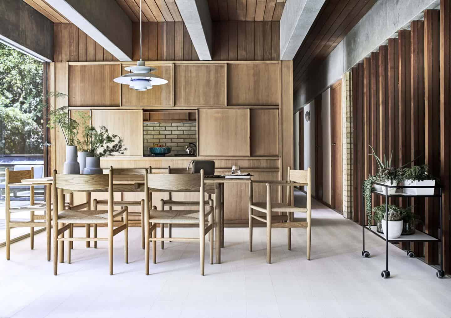 A Japandi style dining room in a mid-century Modern home with floor to ceiling windows, wooden panelling and a Louis Poulsen PH5 Suspension Light