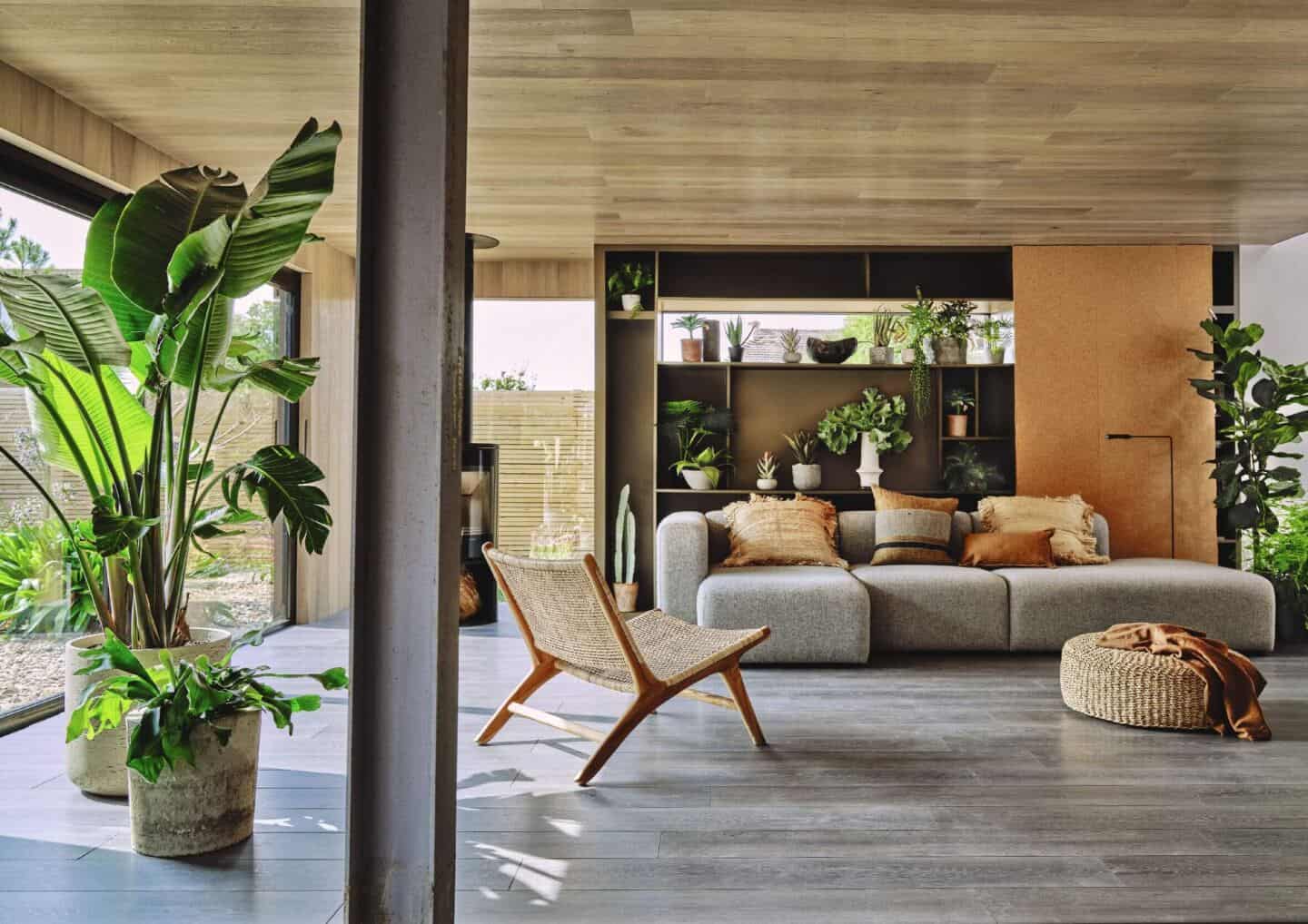 A living room full of natural materials and plants with floor to ceiling windows
