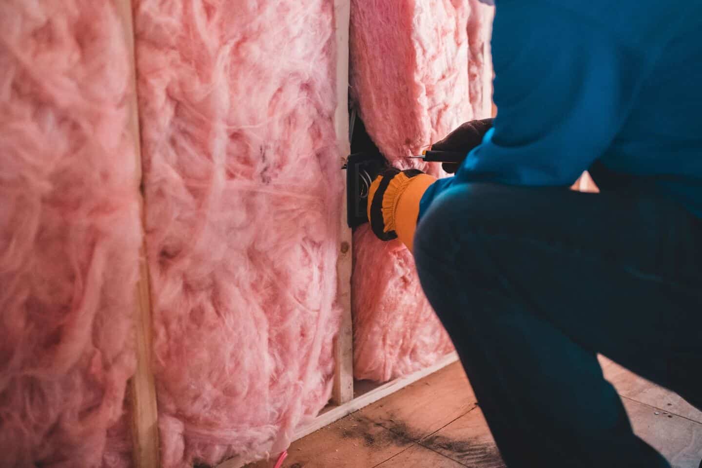 A man fitting pink wall insulation as an eco-friendly home upgrade
