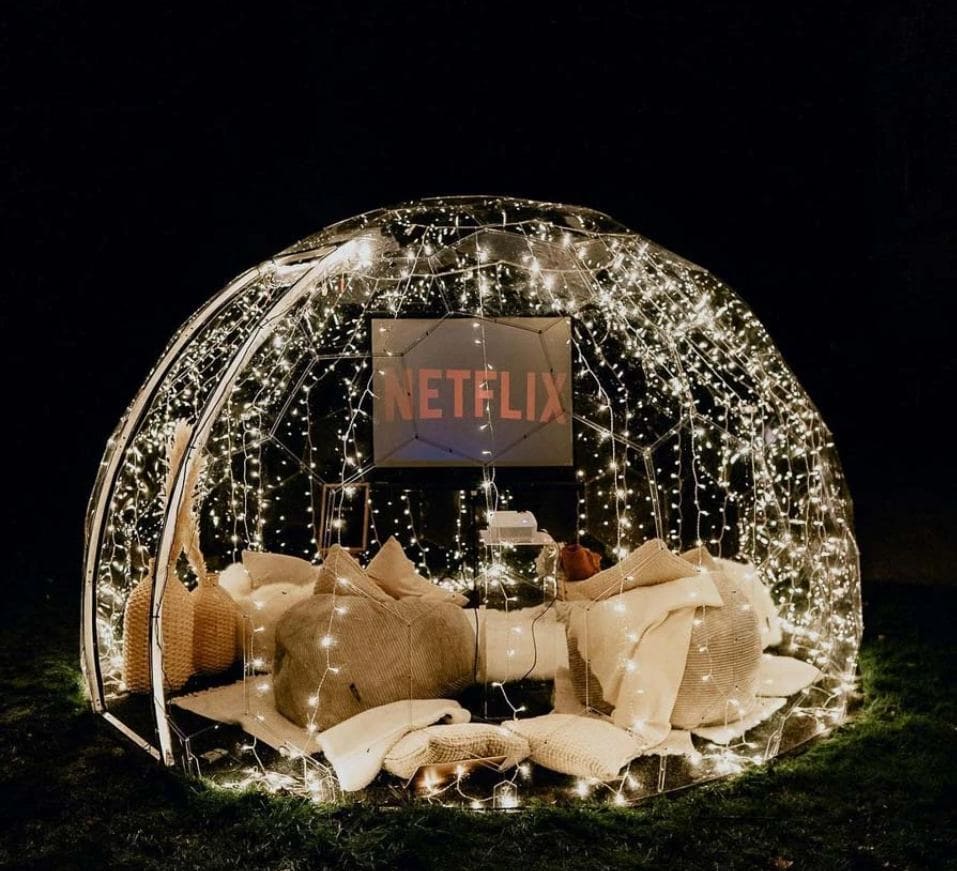 A cosy home cinema set up inside a garden dome with fairy lights draped inside the dome