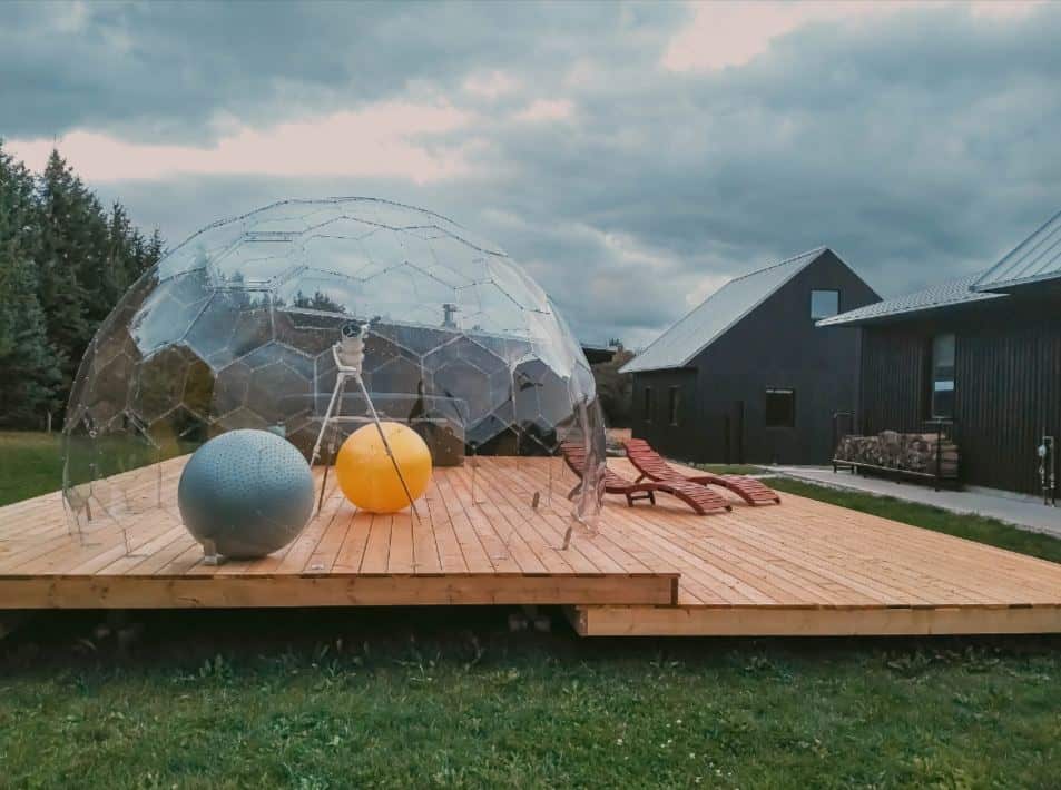 A large telescope and two yoga balls inside a garden igloo on a wooden deck