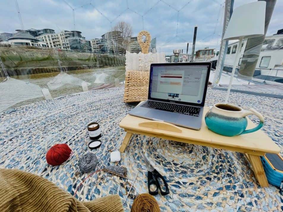 A laptop table with laptop on the floor of a garden igloo. Knitting supplies are on the rug covered floor