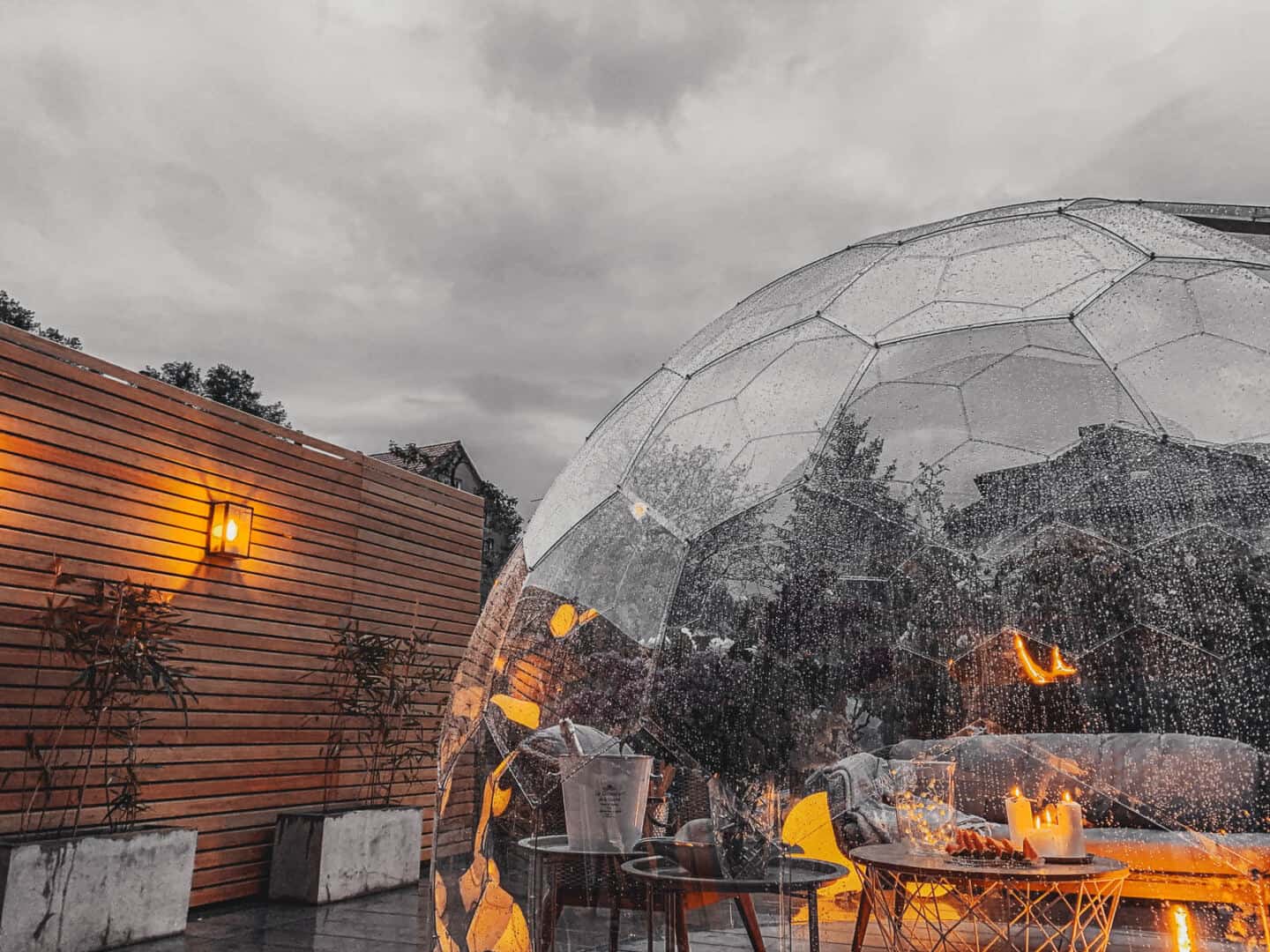 Garden furniture set up inside a garden dome which is covered in rain. Candles and a bottle of champagne create a romantic atmosphere