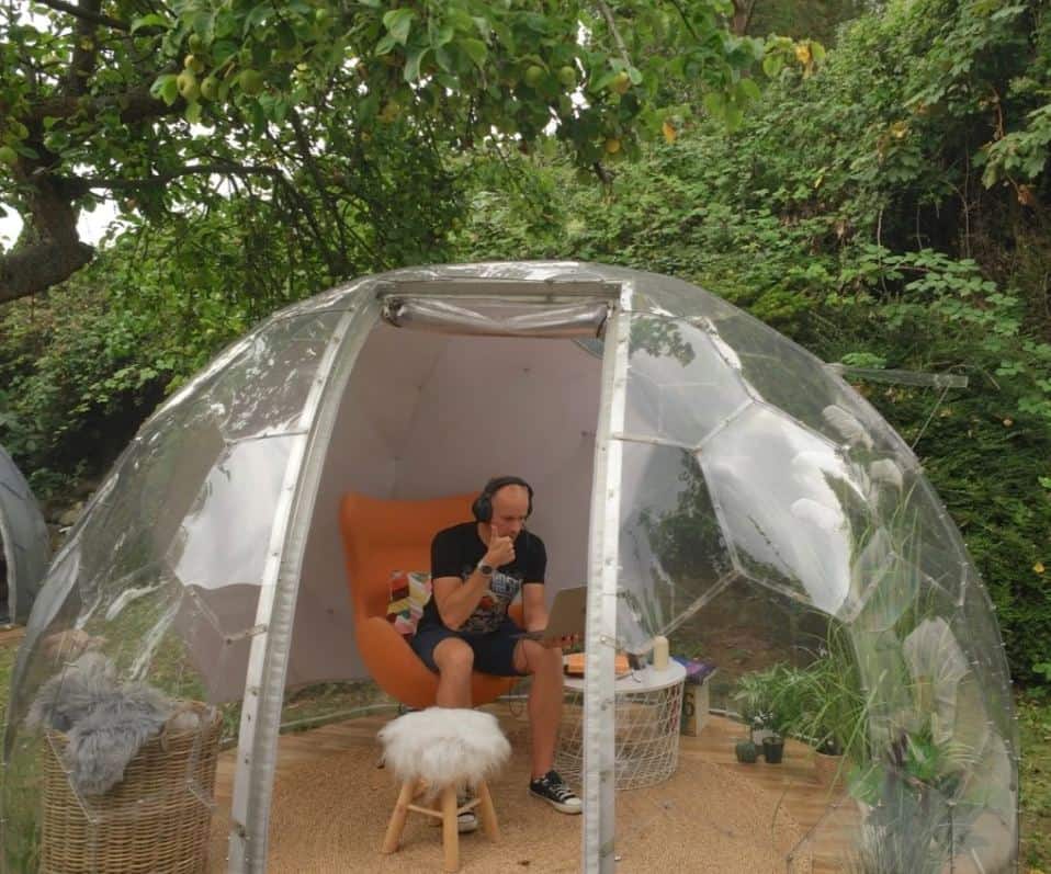 A man wearing headphones looking at a laptop inside a garden igloo