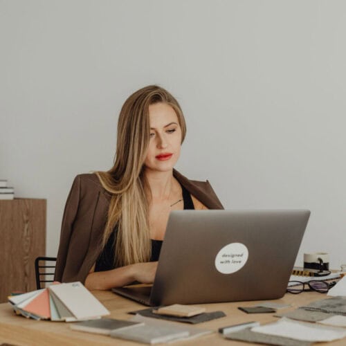 A young female designer or architect sits at her laptop surrounded by colour swatches